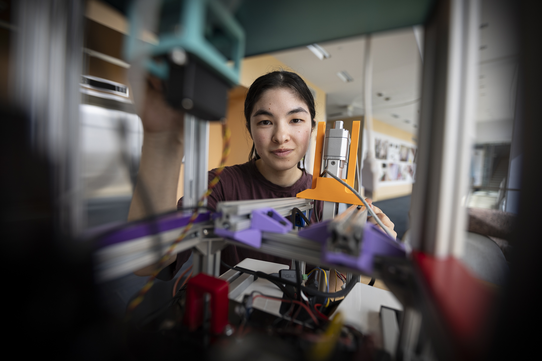 A female Olin College of Engineering student is seen reaching into a 3D printer.