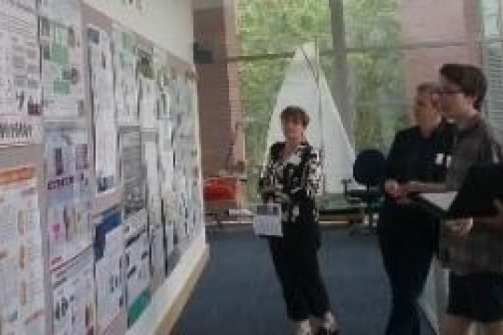A group of people in a hallway looking at a wall of posters of student projects.