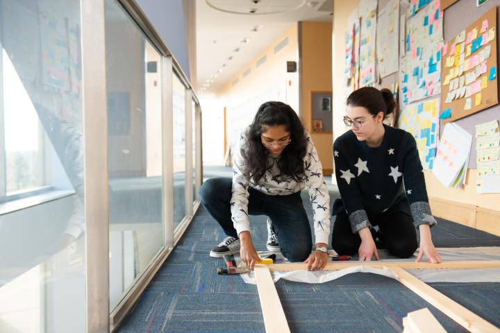 Two students working together on a project that is laid out on the floor.