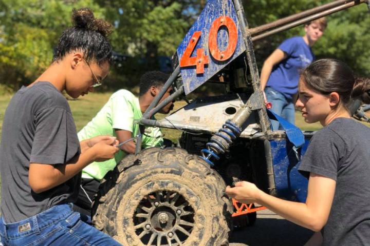 Members of the Olin College Phoenix Racing baja team work on their vehicle A group of engineering students encircle their their off road baja vehicle