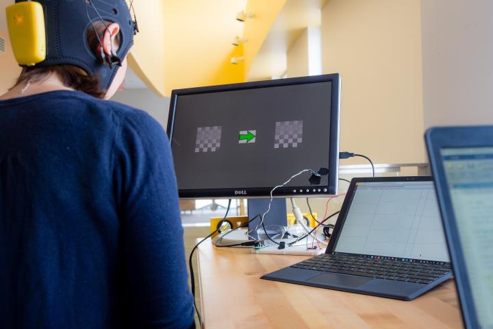 A photo of a person wearing a head covering with electrodes that is connected to a computer