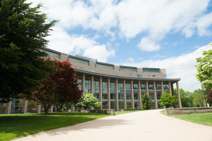 An exterior image of a horizontal-shaped, glass-windowed campus building under a blue, cloudy sky.
