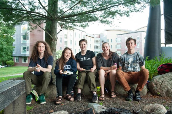 A group of five people sitting on a large rocks under a tree