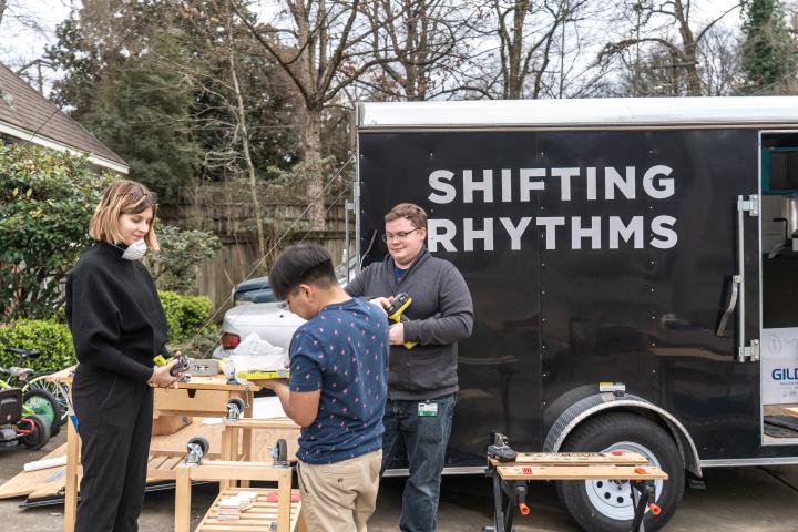 The Shifting Rhythms ADE team hard at work A photo of three students working outside at a workbench with a trailer in the background