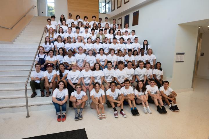 A large group of first year students wearing white tshirts and sitting on graduated steps