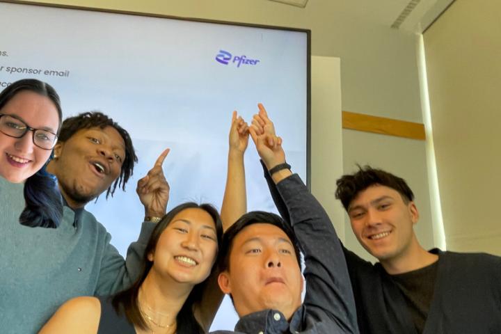 Five students taking a selfie and pointing at Pfizer logo