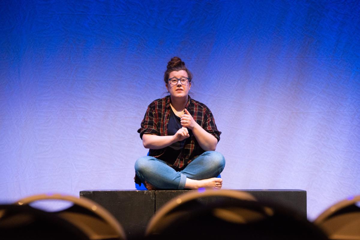 An Olin College student during a class call Storying Ourselves A photo of a person sitting cross-legged on a stage