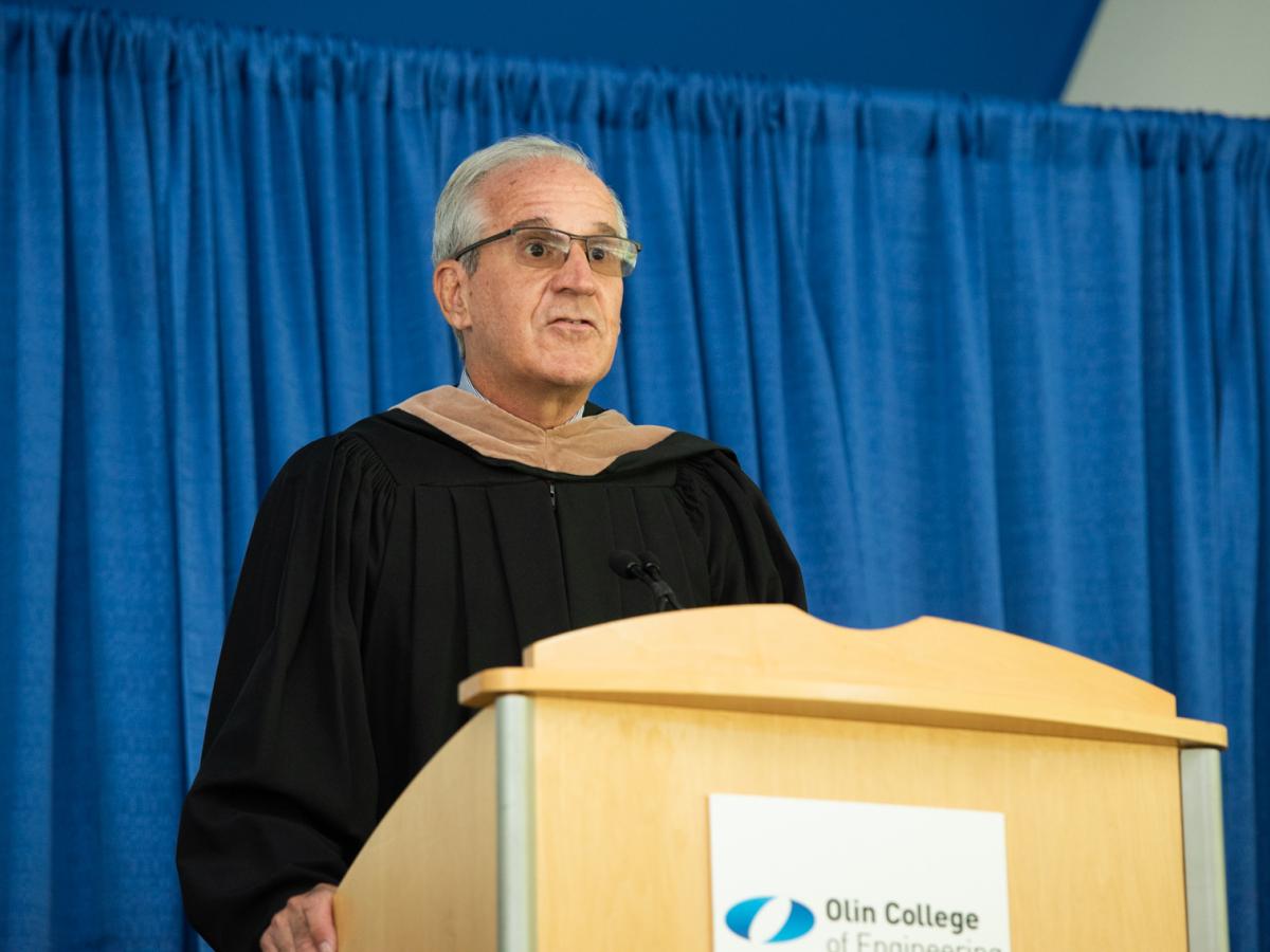 Ken Stokes, Olin College Chair of the Board of Trustees offers the Commencement Greetings Ken Stokes, Olin College Chair of the Board of Trustees stands at a podium and offers the Commencement Greetings