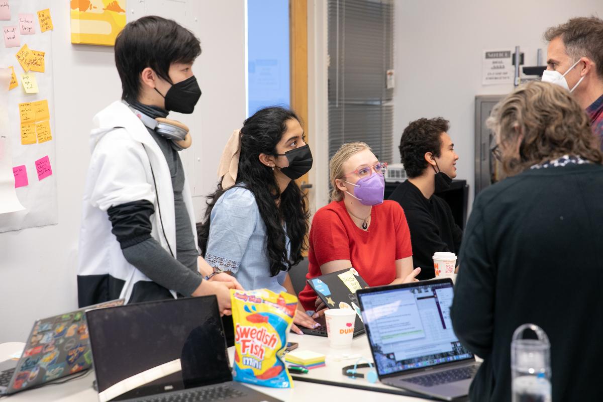 A group of three participants in the STEP course talk with professors. A group of three students wearing face masks talk with professors in a classroom.