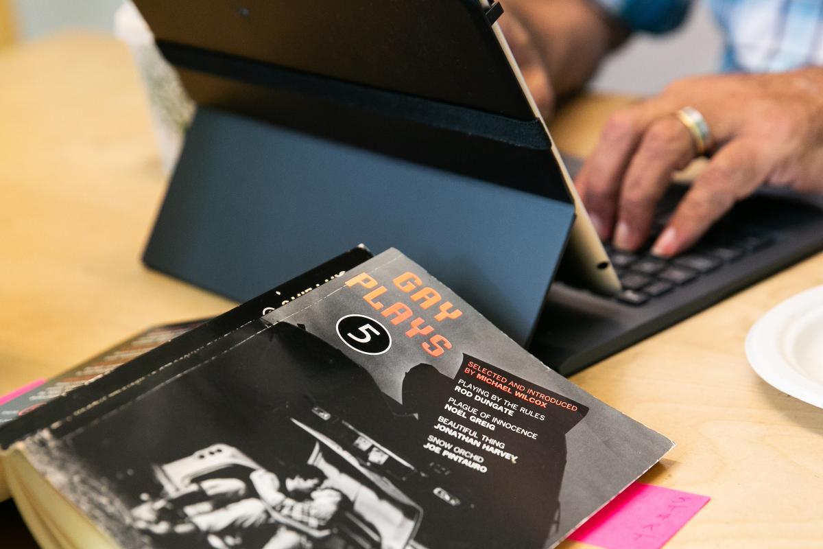 A person types on a laptop during summer Sketch Model 2019. An image of a black book with someone's hands typing on a laptop in the background.