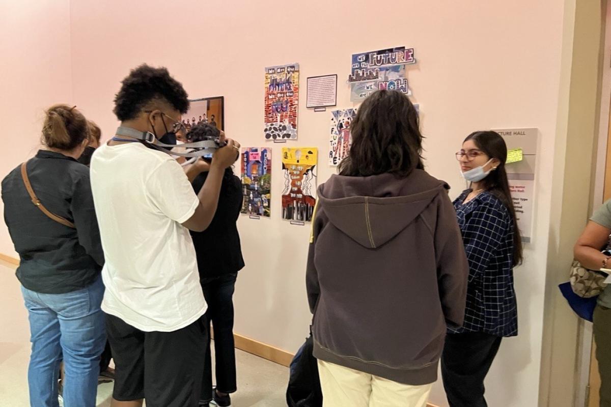 People stand around looking at and taking photos of artwork on a white wall. 