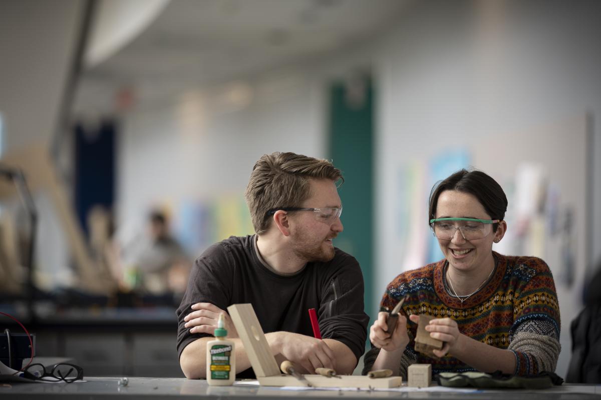 Two students work with wood in the Miller Academic Center (MAC).
