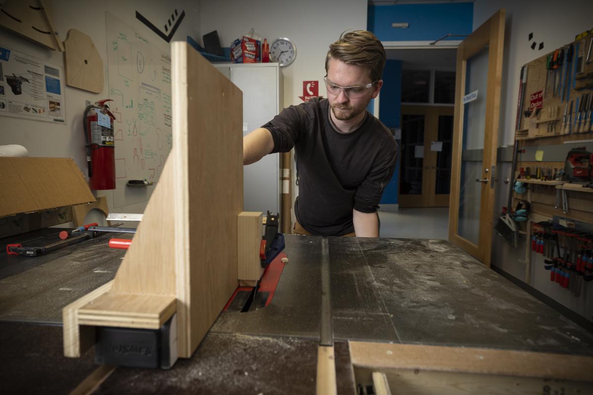 Student cuts a piece of wood on a saw machine. 