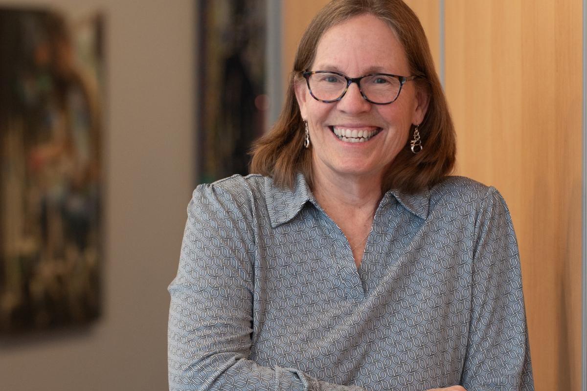 Jeanne Haley, the Senior Director of Counseling, stands in front of a tan wall with artwork in the background. 
