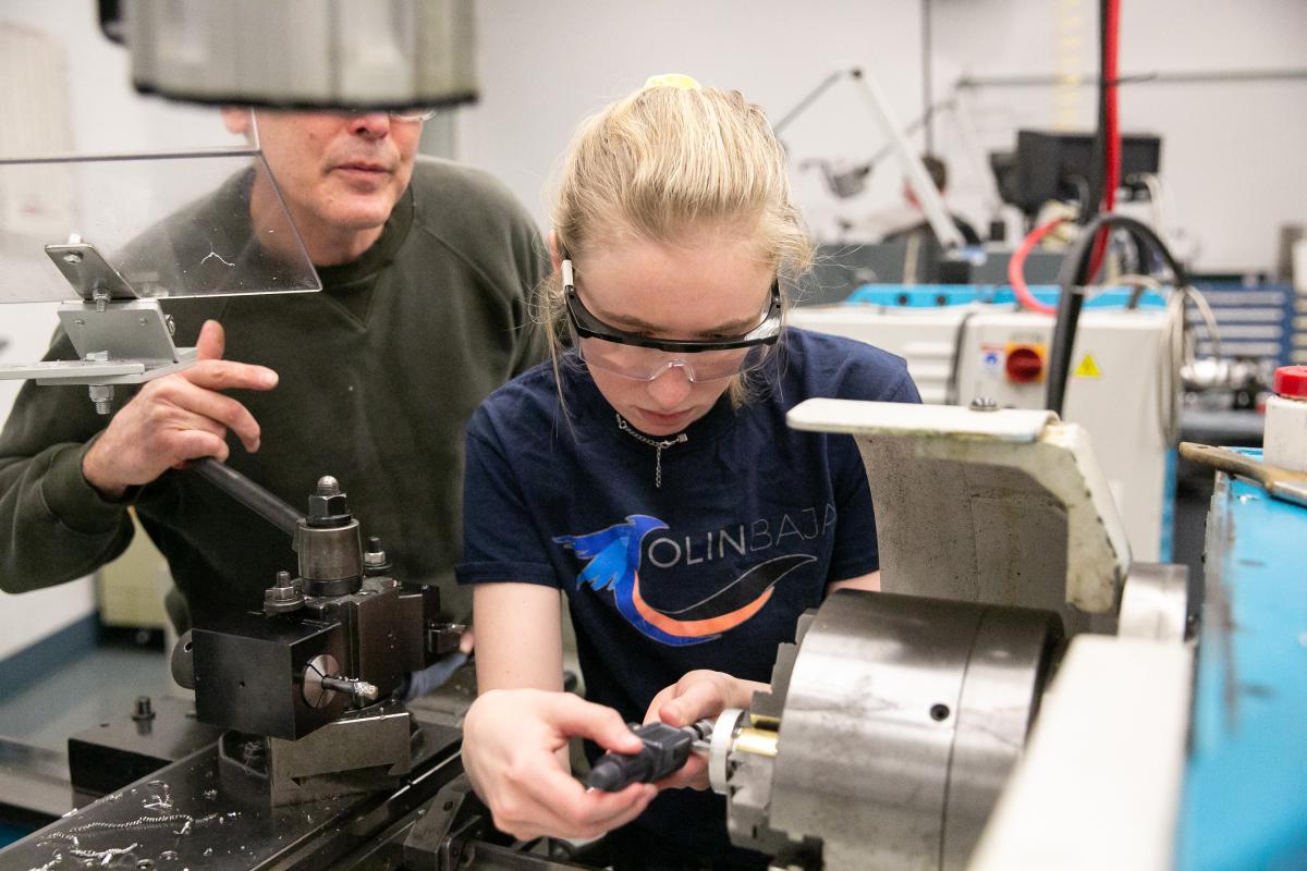 An Olin College student wearing an "Olin baja" t-shirt is shown working in the Olin Shop.