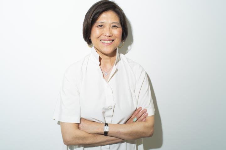 Olin President R. May Lee standing in front of a white background with arms crossed