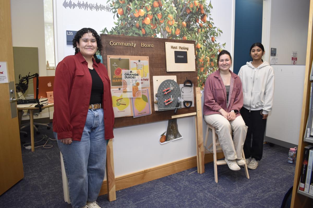Three students stand around their final project. Three students stand around their final project.