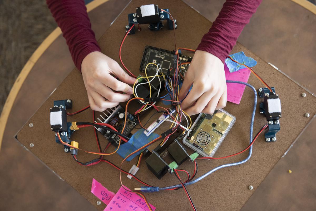 A pair of hands are seen from above working on a project of wires and circuit boards.