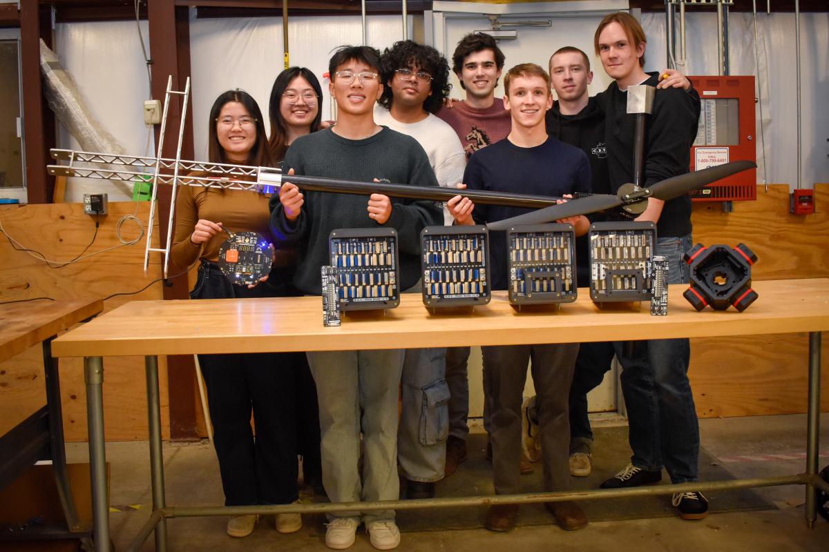 The Olin OCTAL project team members pose together for a group photo. They stand behind a table that holds some of their project components, and also hold some in their hands.