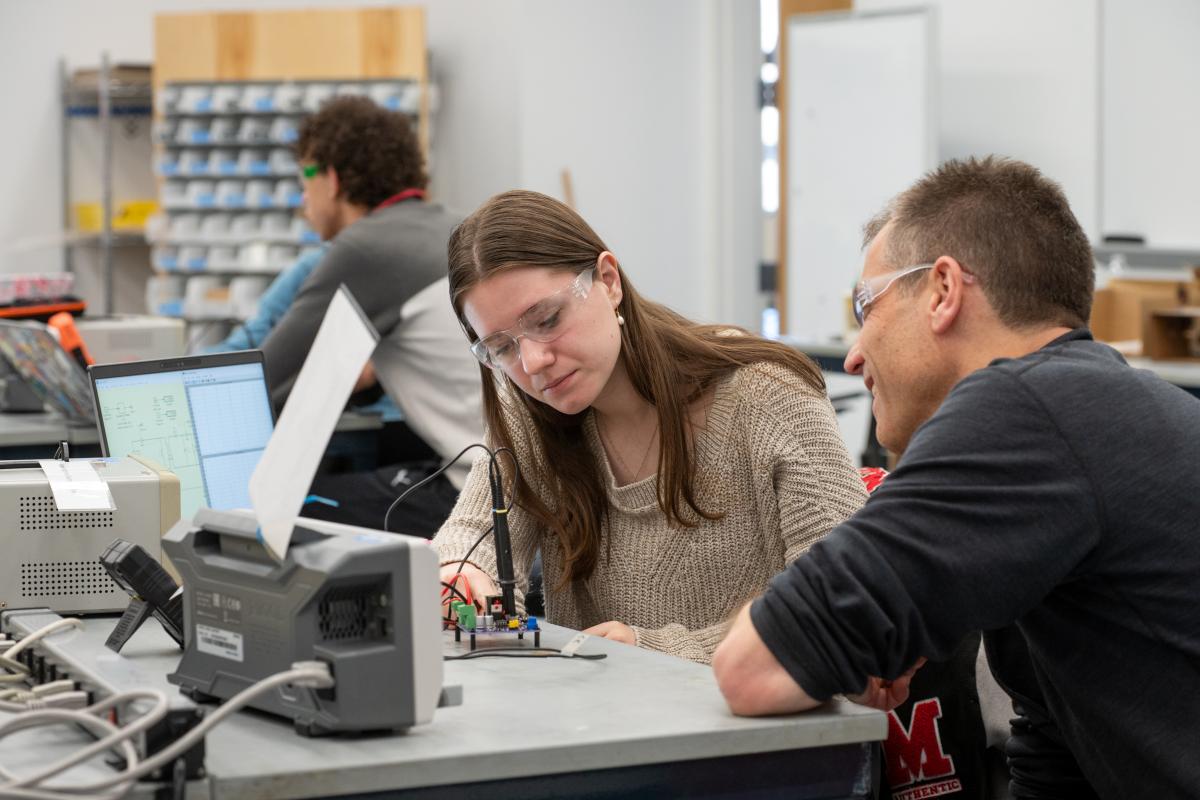 An Olin student wearing safety glasses works with a professor on an electrical engineering project.