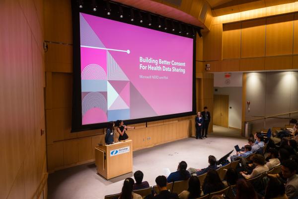 Students presenting slides in packed auditorium 