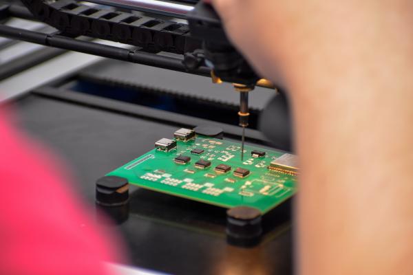 The hands of an Olin OAT project team member are shown working on a circuitboard.