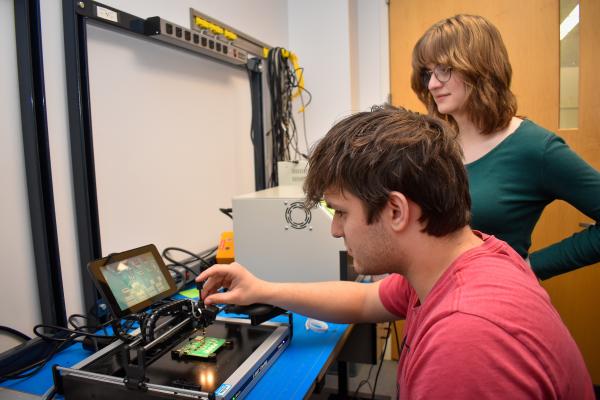 Two Olin OAT project team members, one sitting and one standing, work together on a project.