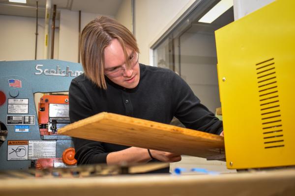 An Olin OCTAL project team member works in the shop with a piece of wood.