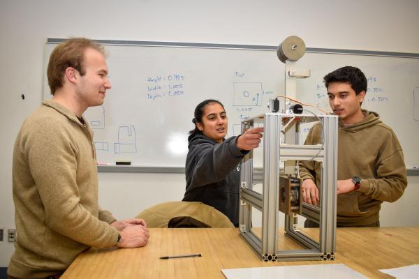 Three Olin OPEL project team members adjust equipment on a classroom table.