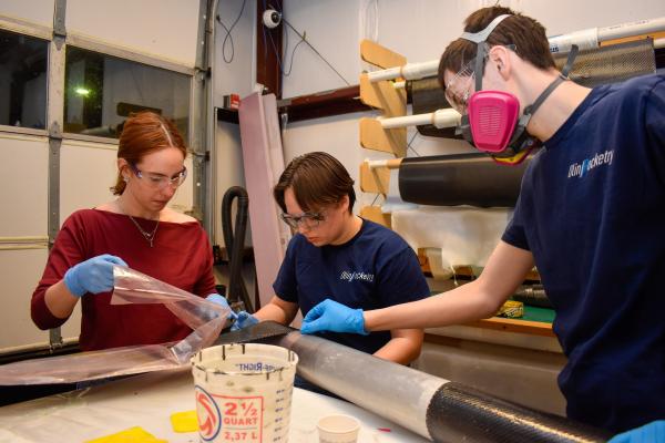 Three Olin Rocketry project team members work together at a workbench in the LPB.